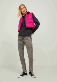 Padded pink jopica preko črne kapuce, sivo ozke kavbojke in črne superge. Jopica ima gumbno zapiranje in puhasto teksturo.