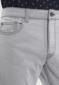 Jeans in denim grigio chiaro con vestibilità slim, dotati di cinque tasche, chiusura con bottone e dettagli di cucitura a contrasto. Texture liscia.
