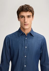 Camicia in denim blu scuro con abbottonatura frontale, colletto classico e maniche lunghe, caratterizzata da semplici bottoni in metallo argentato e un tessuto testurizzato.