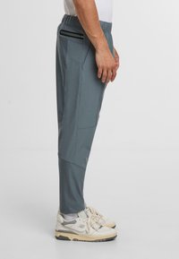 Lätta, smalare idrottsbyxor i skiffergrått, med en elastisk midja, sidofickor med dragkedja och ett glatt tyg med matt yta.