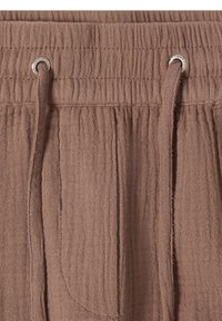 Gros plan d'une ceinture élastique marron avec cordons réglables et œillets métalliques sur tissu texturé.