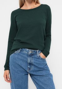 Grön texturerad långärmad topp i kombination med högmidjade ljusblå jeans, med en klassisk rund halsringning och avslappnad passform.