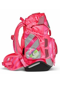 Sac à dos rose vif avec des accents argentés, plusieurs compartiments zippés, des bretelles rembourrées et un badge circulaire présentant un personnage de dessin animé.