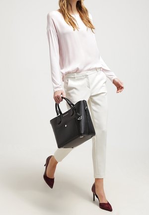 Sac à main en cuir noir avec des poignées supérieures, forme rectangulaire, ferrures en argent, accompagné d'un haut à manches longues rose clair et d'un pantalon blanc.