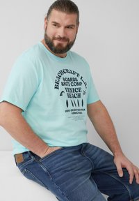 Lichtblauw katoenen t-shirt met een zwarte grafische print met tekst, gedragen met donkerblauwe denim jeans. De stof lijkt zacht en casual.