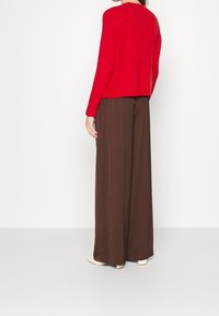 Punainen neulottu neulepaita, jossa on pitkät hihat ja rento istuvuus, yhdistetty korkeavyötäröisiin, leveälahkeisiin ruskeisiin housuihin ja nudenvärisiin kenkiin.