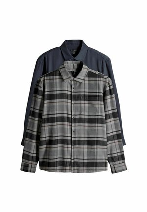 Flannel shirt in gray and black plaid with a chest pocket, layered over a solid blue shirt. Both feature button-up designs and collars.