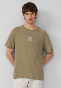 Oliwkowa koszulka z krótkim rękawem, teksturowany materiał, okrągły dekolt, z trzema białymi wzorami desek surfingowych na piersi.