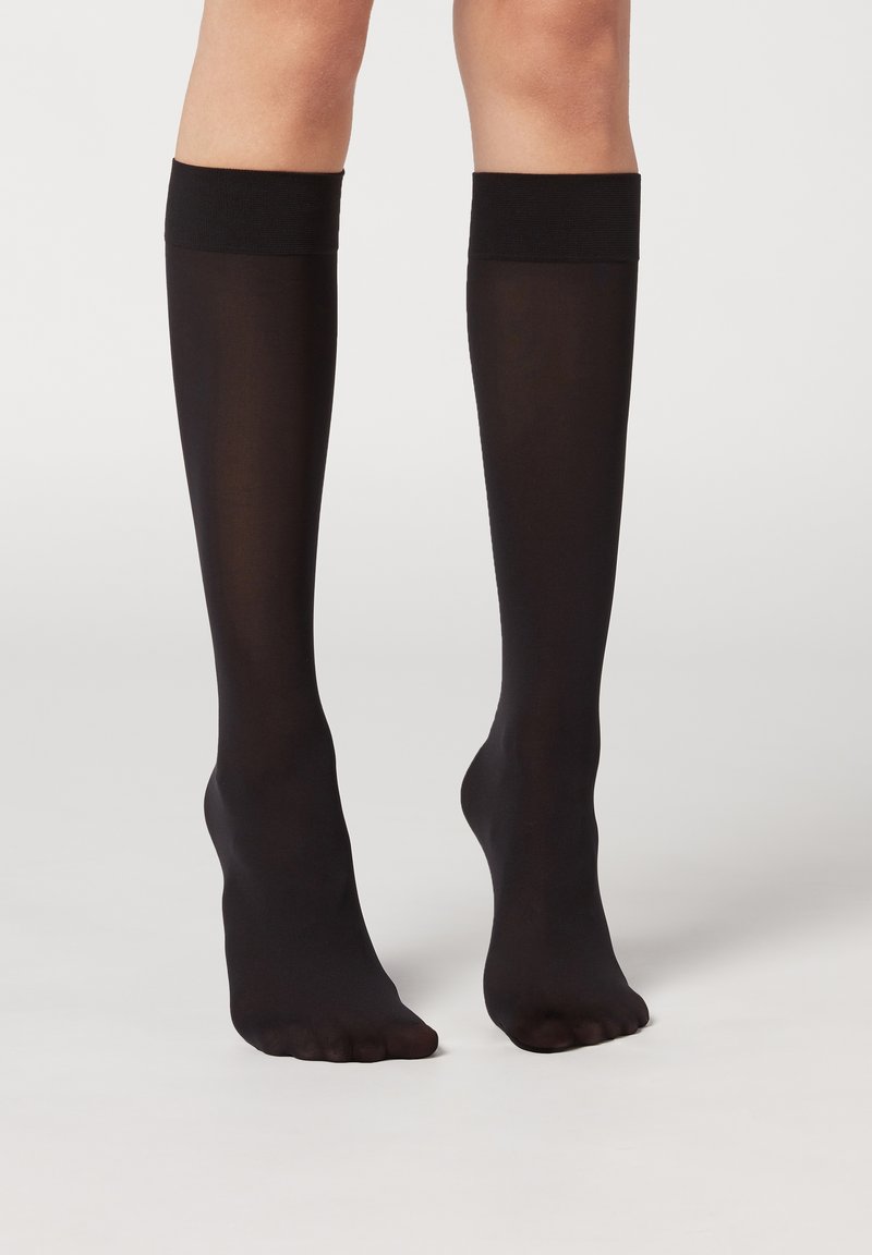 Calze nere fino al ginocchio con una texture liscia e trasparente e una larga banda scura nella parte superiore. Completa vari outfit.