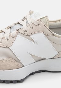 Beige ja valkoinen urheilukenkä, jossa mokkanahkainen ja nahkainen päällinen, teksturoidut nauhat, paksu kumipohja ja näyttävä 'N'-logo.