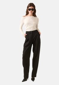 Hosszú ujjú, krémszínű felső, fodros részletekkel, fekete, magas derekú, pliszírozott nadrággal. Fekete, hegyes orrú magassarkú cipővel és napszemüveggel viselve.