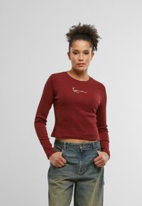 Burgundy long-sleeve crop top with a round neckline and white embroidered design on the chest. Soft ribbed texture; fitted style.