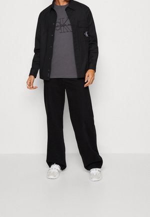 Black button-up shirt over a gray Calvin Klein t-shirt, paired with black corduroy pants and white athletic shoes. Simple design, neutral colors.