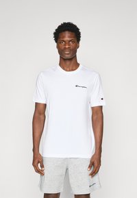 Hvid bomuld T-shirt med korte ærmer, der har et sort "Champion" logo på brystet og et lille logo på ærmet. Enkel design, rund hals.