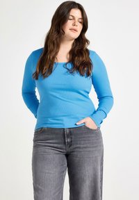 Maglietta a maniche lunghe a costine di un brillante blu, con scollatura quadrata. Abbinata a jeans grigi larghi, evidenziando un look casual.