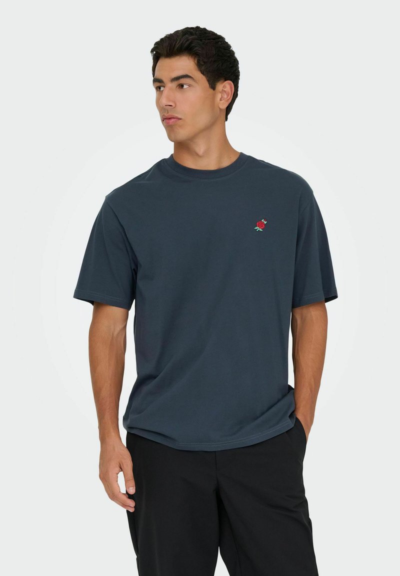 Navyblauwe katoenen t-shirt met een ronde halslijn en korte mouwen, voorzien van een kleine rode rozenborduring op de linkerborst.