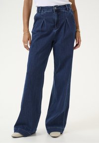 Korkeavyötäröiset, tummansiniset farkut, joissa on leveät lahkeet ja pikeet, napitus edessä, sileä rakenne, hyvin istuva malli ja siisti mate.