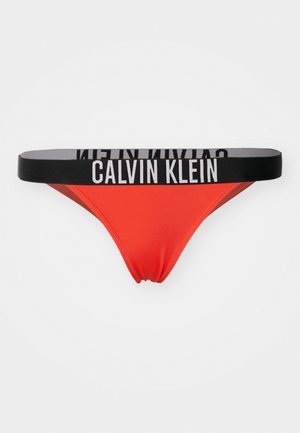 Calvin Kleini string aluspesu erksas punases kangas musta elastse vööga, millel on valge brändinimi. Lihtne, tänapäevane disain.