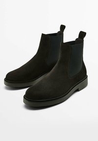 Czarne zamszowe botki typu Chelsea z elastycznymi panelami bocznymi i tylnymi uchwytami, charakteryzujące się grubą podeszwą i przeszyciami wzdłuż krawędzi.
