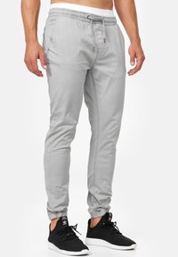 Pantalones jogger de color gris claro con cinta elástica en la cintura, detalle de cordón y puños elásticos; combinados con zapatillas deportivas negras.