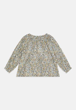 Blouse à manches longues florale en bleu clair, avec un col froncé, ornée de motifs de fleurs jaunes, vertes et violettes sur un tissu texturé.