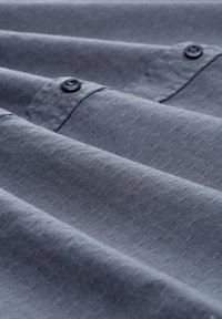 Dunkelblauer, strukturierter Stoff mit subtilen Prägungen und Knopfdetails, die in sanften Falten drapiert sind.