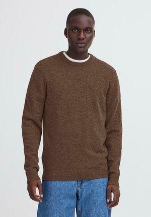 Suéter de punto marrón con cuello redondo, puños y dobladillo acanalados; usado sobre una camisa blanca con cuello; combinado con jeans de mezclilla azul claro.