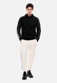 Felpa nera con strisce laterali bianche, abbinata a joggers bianchi con dettagli laterali neri, completata con sneakers nere.