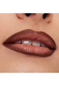 Close-up of lips with smooth brown matte lipstick and slightly parted teeth visible, skin tone light and natural.