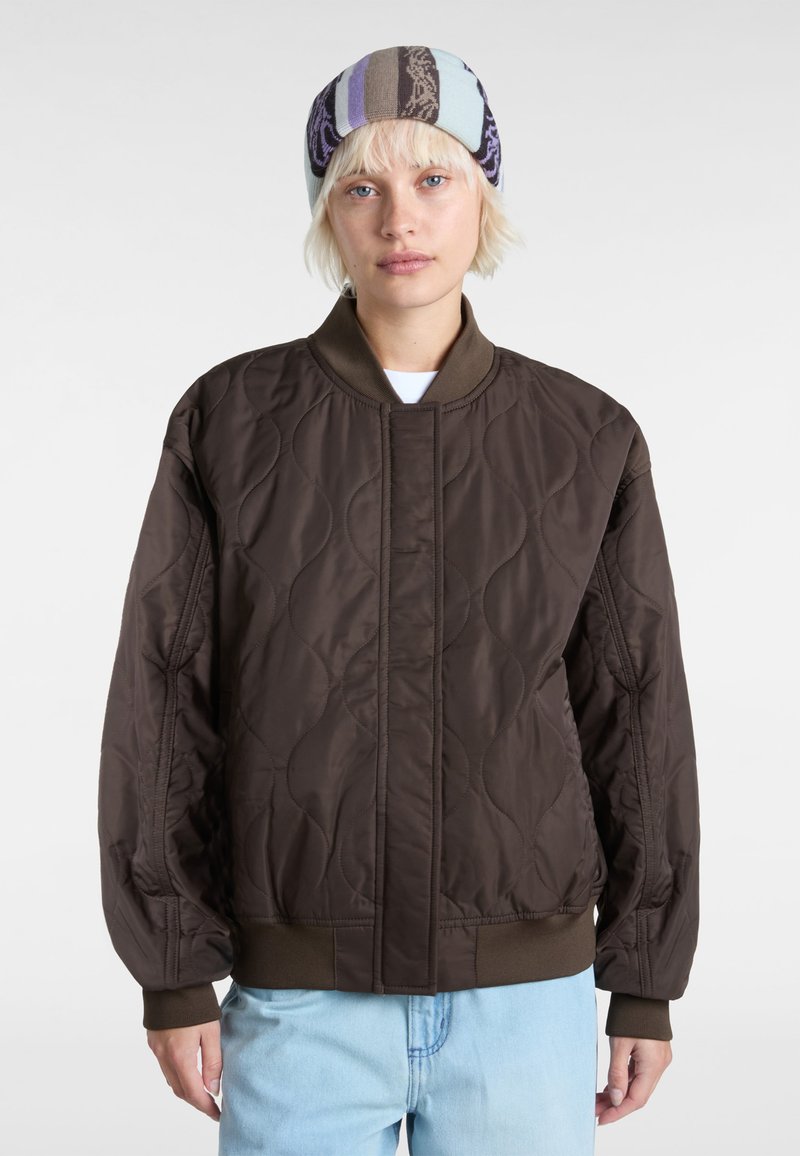 Braune gesteppte Bomberjacke mit geripptem Kragen und Bündchen, die eine glatte Textur und subtile wellenförmige Muster auf dem Stoff aufweist.