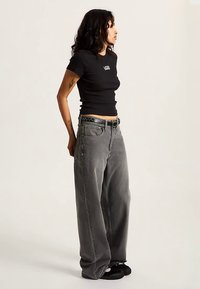 Svart ribbad kortärmad tröja med vit logotyp, kombinerad med löst sittande grå denimjeans med slitna detaljer och ett svart bälte.