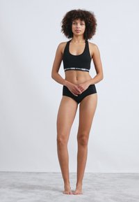 Fekete sportmelltartó, kerek nyakkivágással és logós pánttal, összeillő fekete alsóneművel párosítva. Sima anyag, minimalista dizájn, testhezálló fazon.