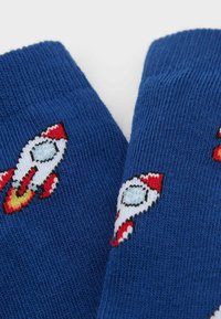 Blå sokker lavet af strikket stof, med broderede raketdesigns i rød, hvid og blå, samt en ribbet struktur øverst.