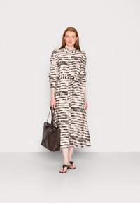 Vestido midi de manga bufante em tecido leve com um padrão abstrato em preto e branco, atado na cintura. Acompanhado por uma bolsa de mão escura.
