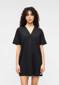 Μαύρο βαμβακερό φόρεμα με κοντά μανίκια, λαιμόκοψη σε σχήμα V και ευθεία γραμμή. Ομαλή υφή, μήκος μέχρι το γόνατο, με κεντρική ραφή στο μπροστινό μέρος.