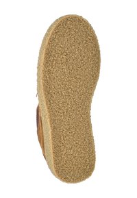 Suela de un zapato de ante marrón con una superficie de agarre de goma beige y texturizada, mostrada desde la parte inferior sobre un fondo blanco.
