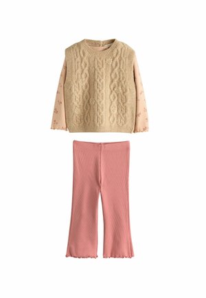 Beige kabelstrik sweater lagd over en rosa langærmet top med blomstermønster; parret med rosa ribbet flared bukser med bølget kant.