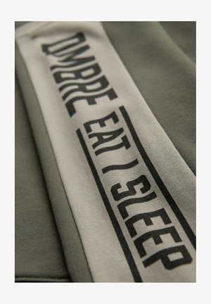 Zielona bluza z haftowanym kremowym paskiem z czarnym napisem "OMBREEAT/SLEEP" w różnych stylach czcionek. Miękka tekstura i swobodny design.