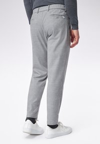 Pantaloni grigi a scacchi realizzati in tessuto intrecciato, con una tasca posteriore e un design aderente. Abbinati a sneakers bianche.