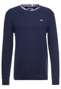 Navy sininen neulepusero, jossa on pyöreä kaula-aukko ja musta-valkoinen ribbineck. Pienen logo rinnan kohdalla. Pitkät hihat, tekstuurinen kangas.