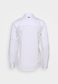 Camicia bianca con bottoni, maniche lunghe, colletto standard e orlo curvo. Tessuto di cotone liscio con una piccola etichetta con logo sul collo.
