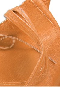 Sac en cuir tan avec une surface texturée, doté de longues et fines sangles et d'un intérieur lisse. Forme arrondie avec des détails de couture visibles.