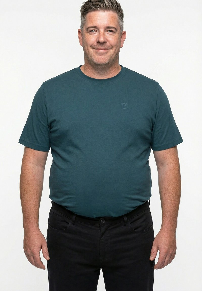 Koszulka z krótkim rękawem i okrągłym dekoltem w kolorze morskim; posiada subtelne logo "B". W połączeniu z ciemnymi spodniami, uwaga skupiona na gładkiej fakturze góry.