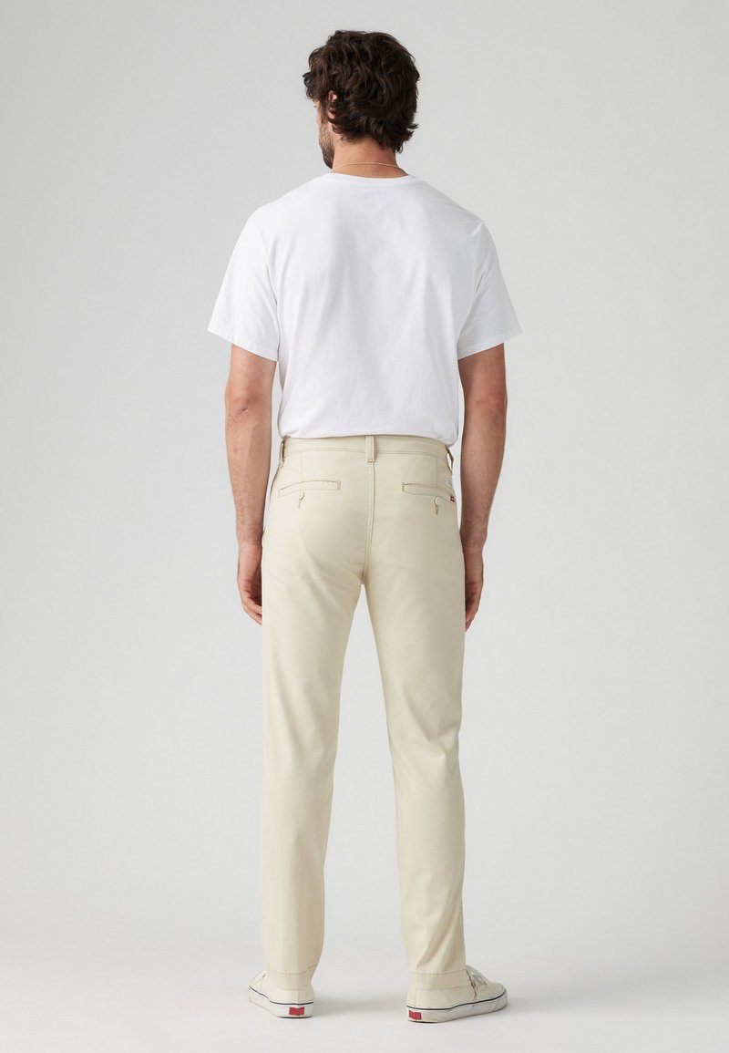 Chinos beige con un corte recto, hechos de una mezcla de algodón, que cuentan con bolsillos traseros y una cinturilla con pasadores para cinturón.