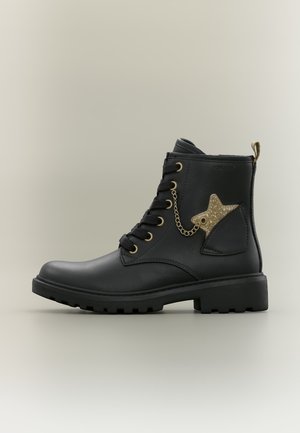 Bottine noire à lacets avec semelle robuste et charm étoile dorée pailletée attaché par une petite chaîne sur le côté.
