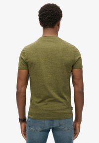 Olivenfarvet t-shirt med korte ærmer lavet af struktureret stof, med rund halsudskæring, tætsiddende pasform og et lille logo mærke ved taljen.