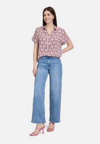 Blusa a maniche corte con un design a motivi rossi e blu, abbinata a jeans a gamba larga di colore azzurro chiaro e sandali con tacco rosa.