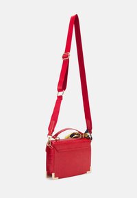 Sac à main en cuir rouge imitation crocodile avec une bandoulière rouge amovible, une quincaillerie dorée et un foulard en soie à motifs en accent sur la poignée.