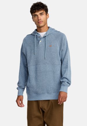 Light blue hooded sweatshirt in soft material with a textured design, featuring a two-button neckline and drawstrings. Paired with brown pants.