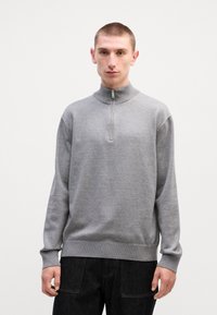 Grauer Zip-Hoodie mit hohem Kragen, weichem Material und gerippten Bündchen. Schlichtes Design mit kleinem Logo auf der Brust.